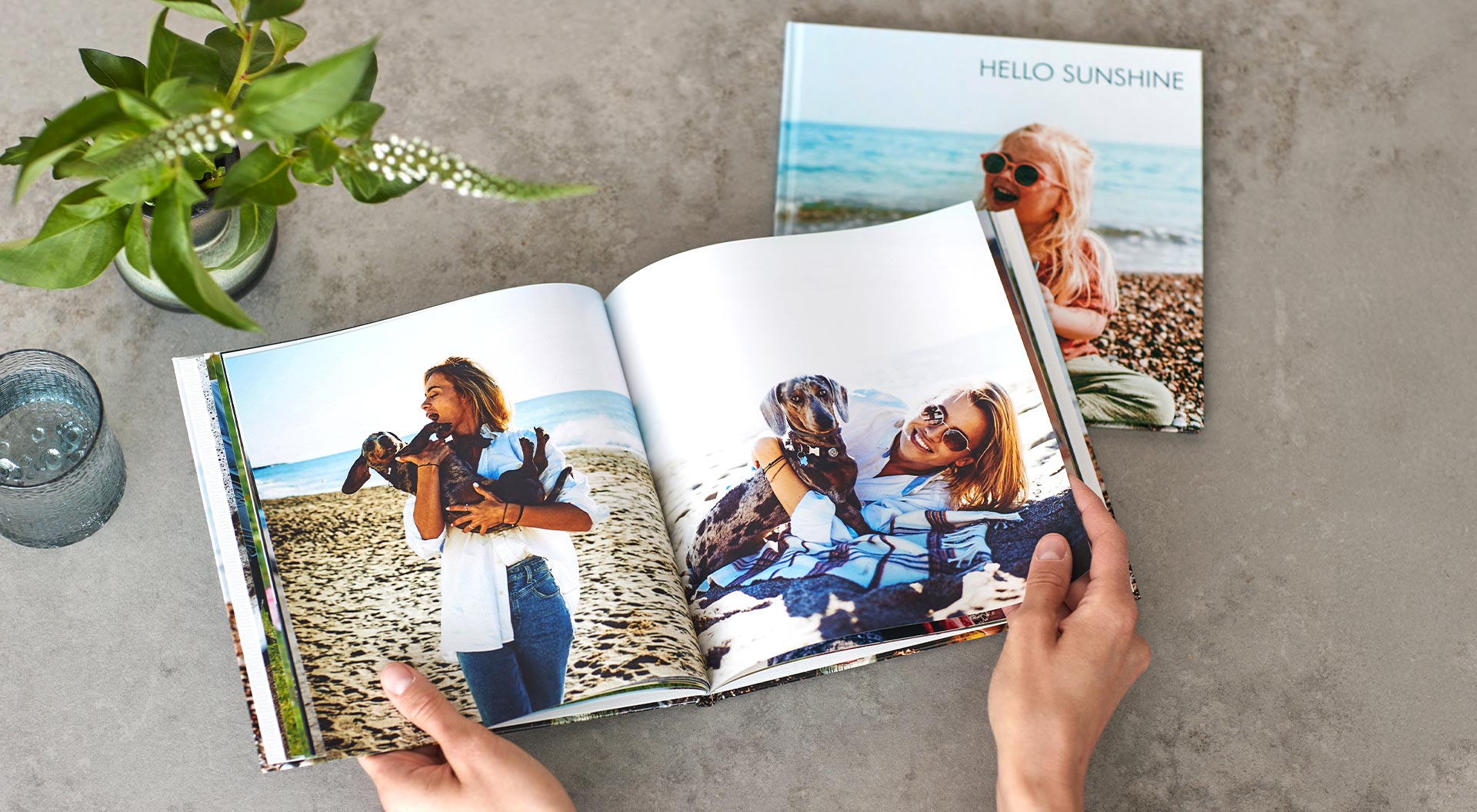 Hands leafing through a square-shaped photo book. The pictures show a woman and a dog on the beach.