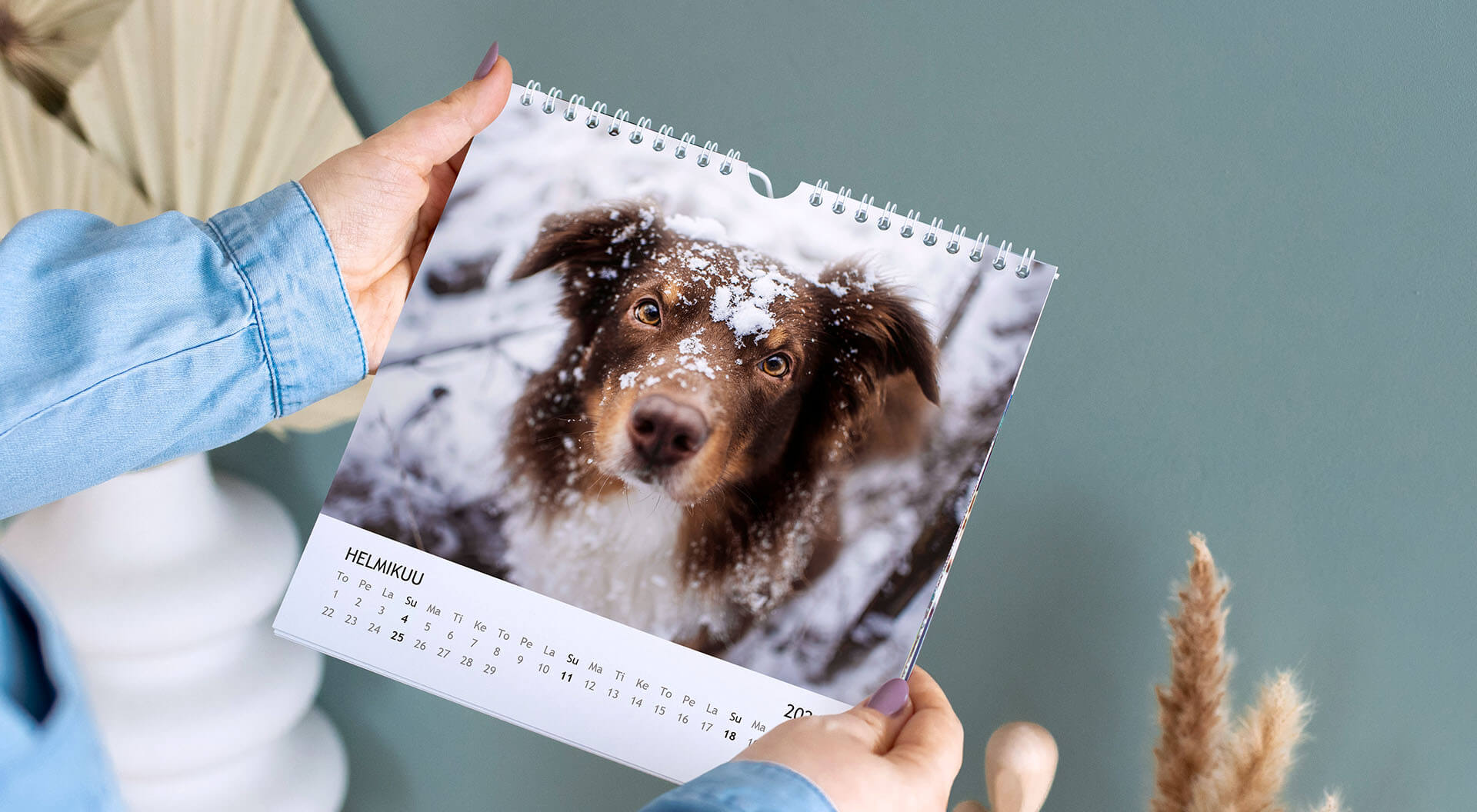 Henkilö pitää kädessään neliönmuotoista seinäkalenteria jossa kuva koirasta