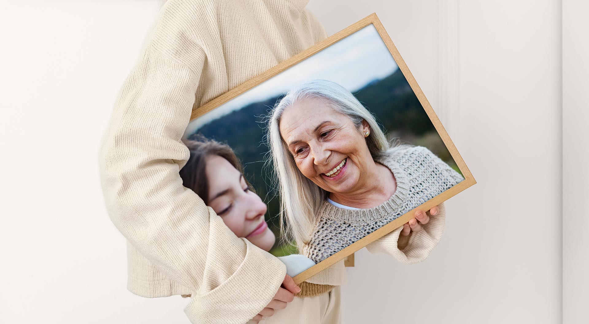 En person håller en inramad canvas-tavla med en bild av en mormor med ett vuxet barnbarn