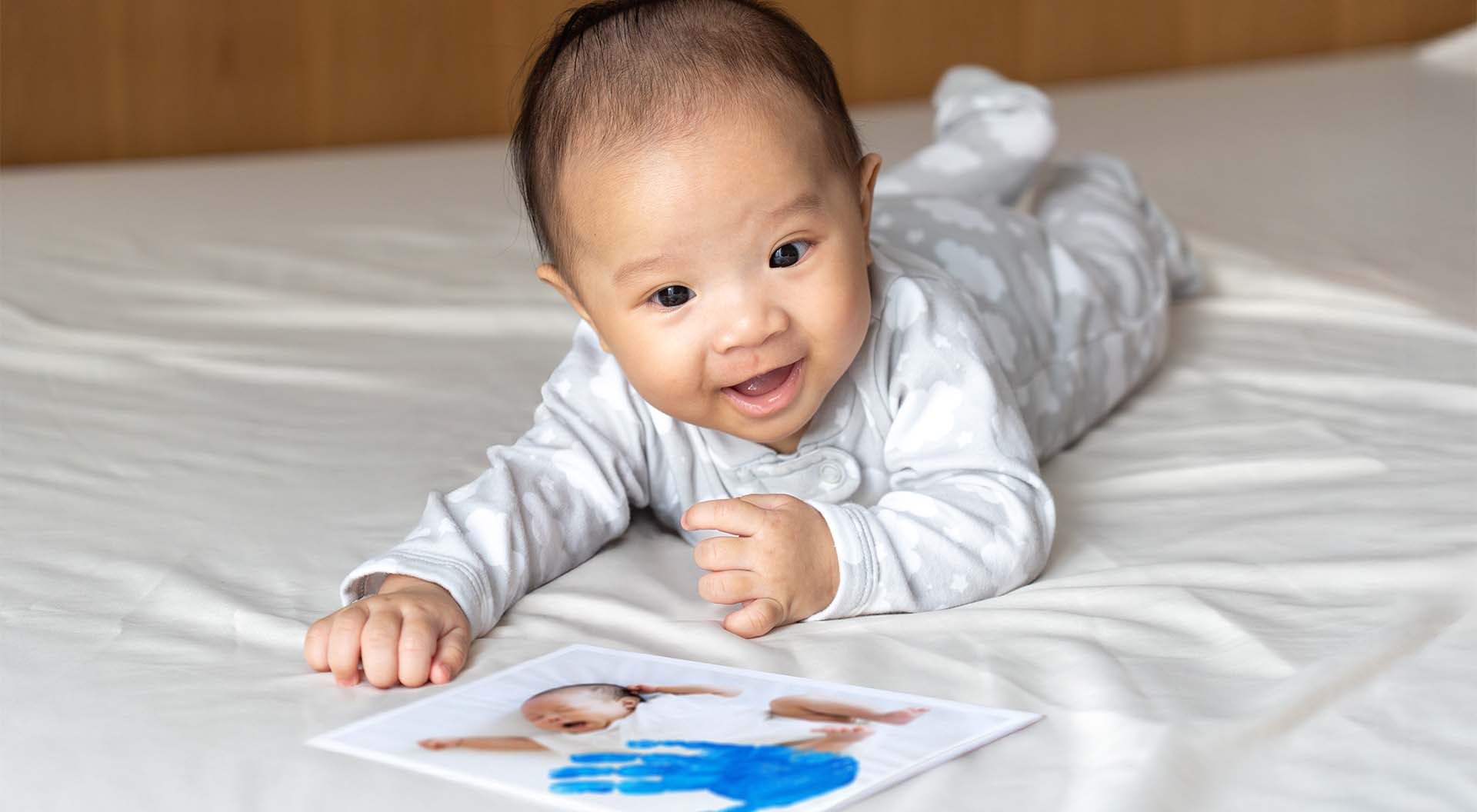 En bebis som ligger på mage, bredvid ett kort med barnets handavtryck